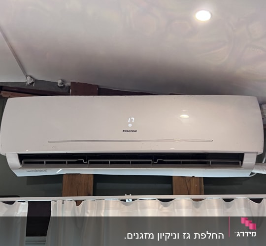 מזגן קיר לבן מותקן על קיר עם וילון לבן